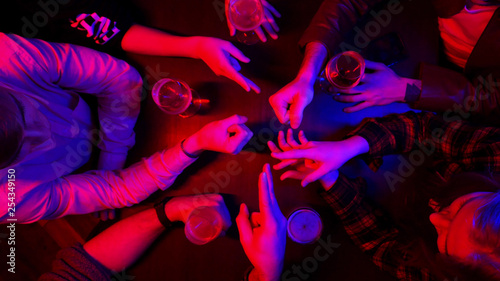 Bar with neon lighting. Group of friends spending time together drinking. Playing Rock Paper Scissors