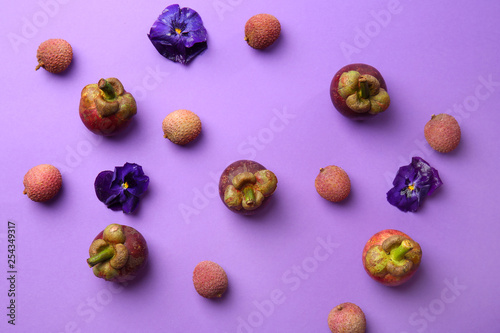 Tasty mangosteen with litchi and flowers on color background