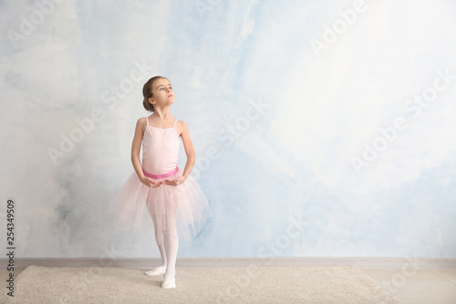 Cute little ballerina near light wall