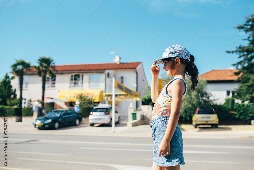 A pretty cute little girl in a beautiful summer suit stands by the parking