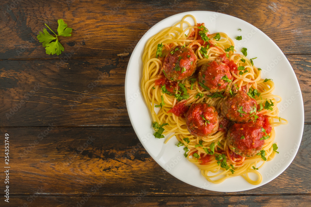 Pasta and meatballs with mozzarella, tomato sauce, fresh parsley, white plate on wooden rustic table, top view