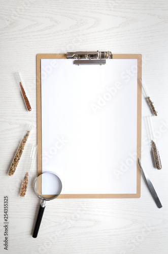 Vertical shot.Clipboard with blank paper and test tubes with different kinds of seed,magnifying glass on white table.Concept of laborotory testing seeds photo