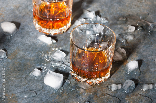 Two old fashioned glasses with whisky and ice cubes on bar counter. Hard light and shadows