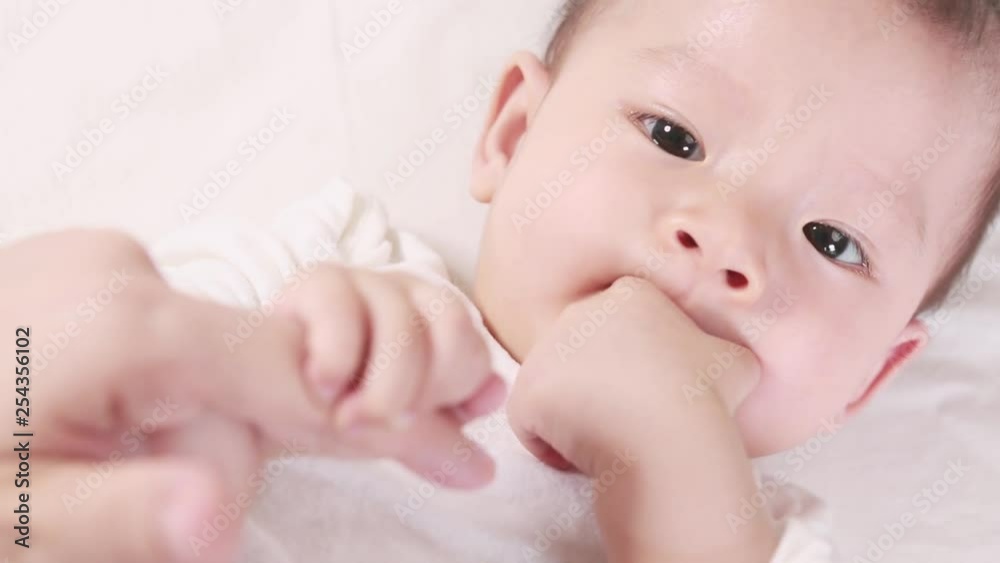 Cute asian baby sucks the thumb and lying on the bed with her mom, New family and baby healthy concept Cute asian baby sucks the thumb and lying on the bed with her mom, New family and baby healthy concept