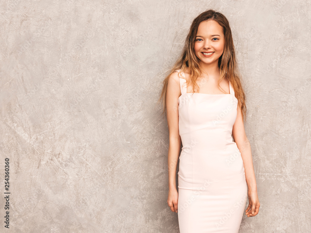 Portrait of young beautiful smiling hipster girl in trendy summer light pink dress. Sexy carefree woman posing near gray wall. Positive model having fun Portrait of young beautiful smiling hipster girl in trendy summer light pink dress. Sexy carefree woman posing near gray wall. Positive model having fun