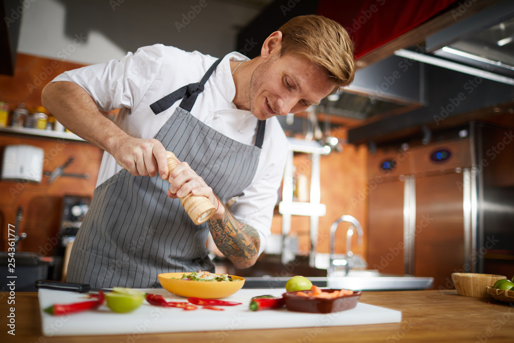 Portrait of handsome professional chef salting dish while cooking in restaurant kitchen, copy space Portrait of handsome professional chef salting dish while cooking in restaurant kitchen, copy space
