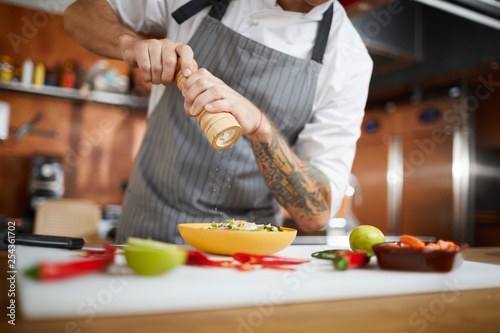 Photography Mid section portrait of professional chef salting dish while cooking in restaura