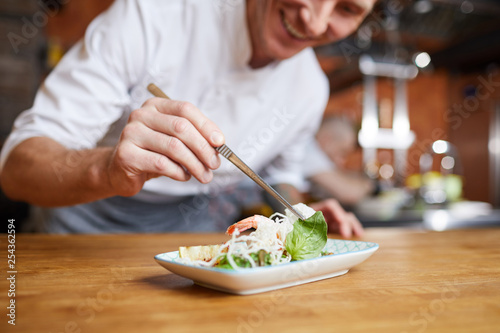 Fototapeta Closeup of professional chef plating Asian dish in restaurant kitchen, copy spac