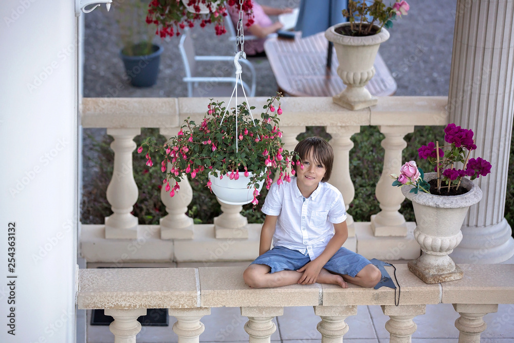 Sweet preschool boy, holding welcome sign in french, sitting on a railing in garden Sweet preschool boy, holding welcome sign in french, sitting on a railing in garden