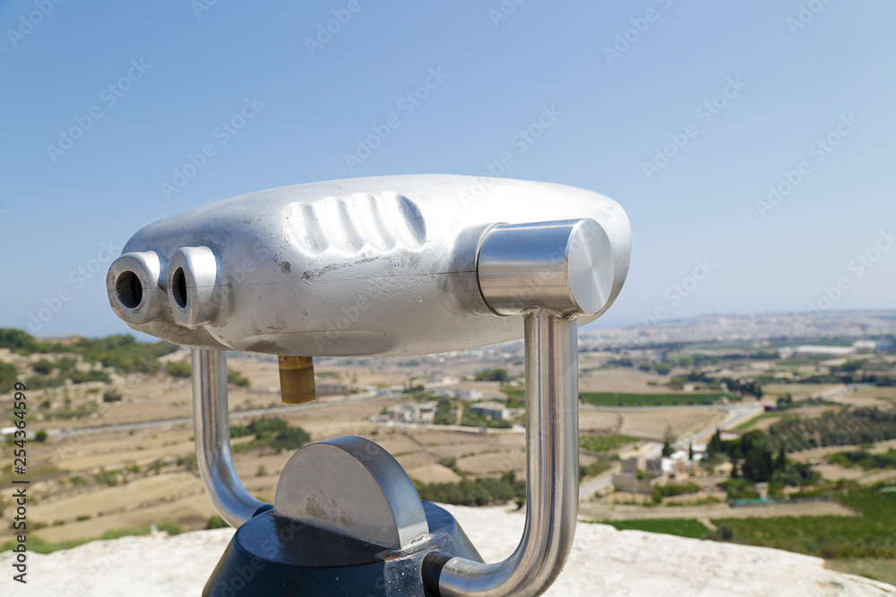 In the foreground a coin operated telescope in the background a view of the city of Mdina, Malta