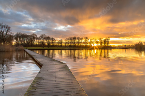 Wooden walkway in lake under orange sunset © creativenature.nl