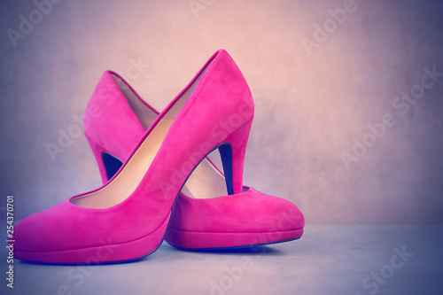 Bright pink high-heeled shoes on gray background.