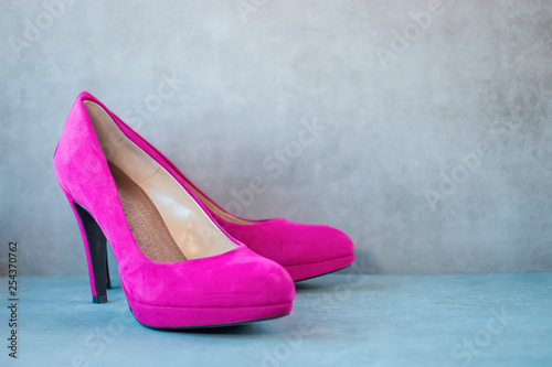 Bright pink high-heeled shoes on gray background.