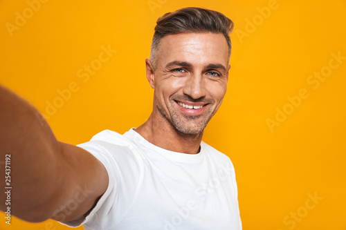 Image of joyful man 30s in white t-shirt smiling and taking selfie photo