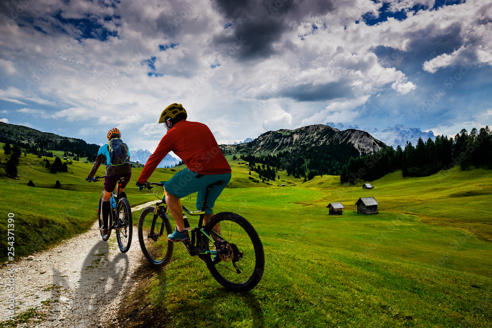 Obraz premium Cycling woman and man riding on bikes in Dolomites mountains andscape. Couple cycling MTB enduro trail track. Outdoor sport activity.