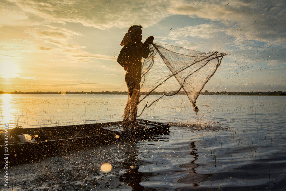 Asia fisherman using net fishing on wooden boat casting net sunset