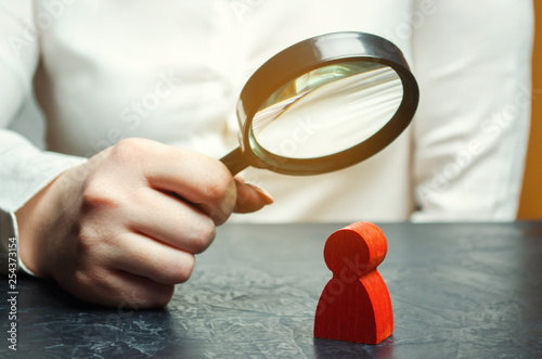 Business woman examines a red man's figure through a magnifying glass. Analysis of the personal qualities of the employee. Characteristic. Unreliable employee. Toxicity in the staff of workers photo