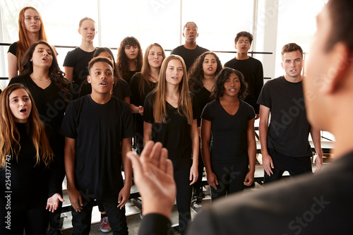 Fototapeta Male And Female Students Singing In Choir With Teacher At Performing Arts School