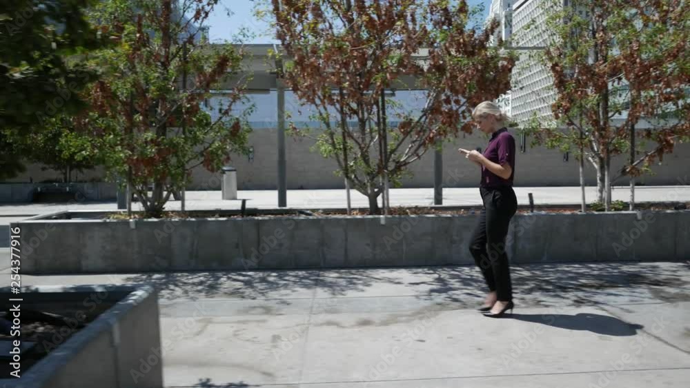 Wide profile of young woman walking through a city while on her smartphone. Wide profile of young woman walking through a city while on her smartphone.