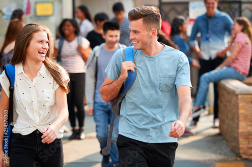 Group Of Smiling Male And Female College Students Walking And Chatting Outside School Building