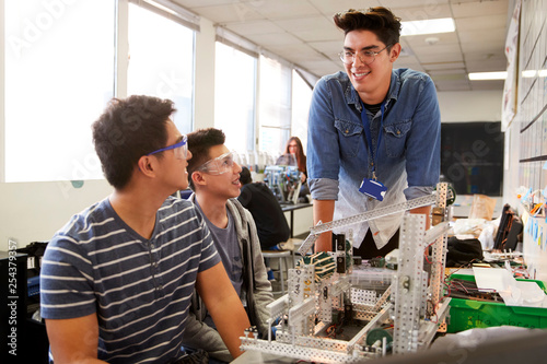 Teacher With Two Male College Students Building Machine In Science Robotics Or Engineering Class