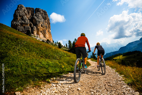 Cycling woman and man riding on bikes in Dolomites mountains landscape. Couple cycling MTB enduro trail track. Outdoor sport activity.