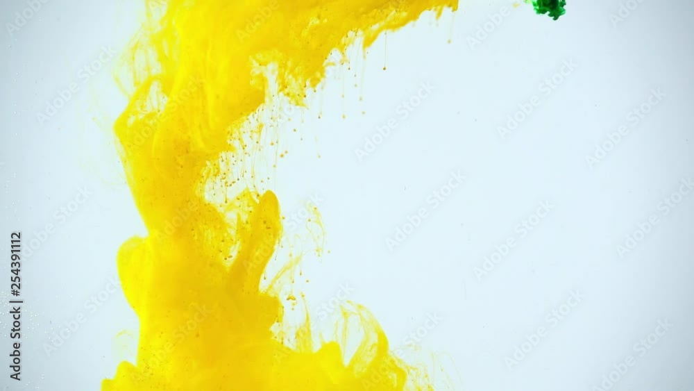 slow motion shoot of green and yellow paints dissolving in water on grey background