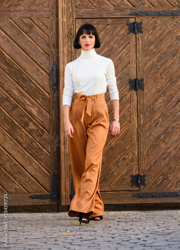 Fashionable outfit slim tall lady. Woman confidently walk. Woman fashionable brunette stand outdoors wooden background. Fashion and style concept. Girl with makeup posing in fashionable clothes