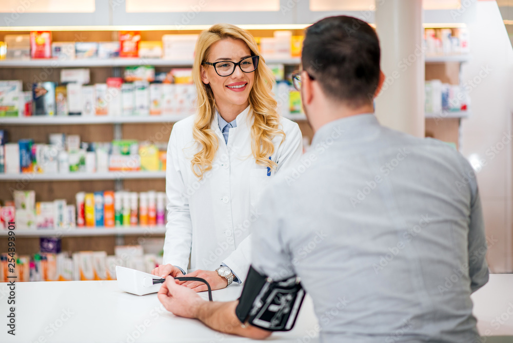 Male customer getting his blood pressure measured by a friendly healthcare worker in hospital pharmaceutical store.