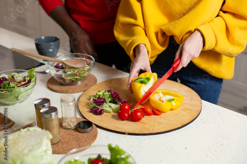 Close up of two people standing near the kitchen table and cutting vegetables
