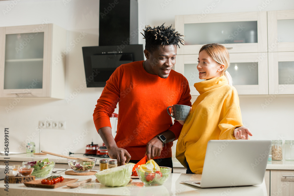 Lady pointing to the laptop while standing with boyfriend in the kitchen Lady pointing to the laptop while standing with boyfriend in the kitchen