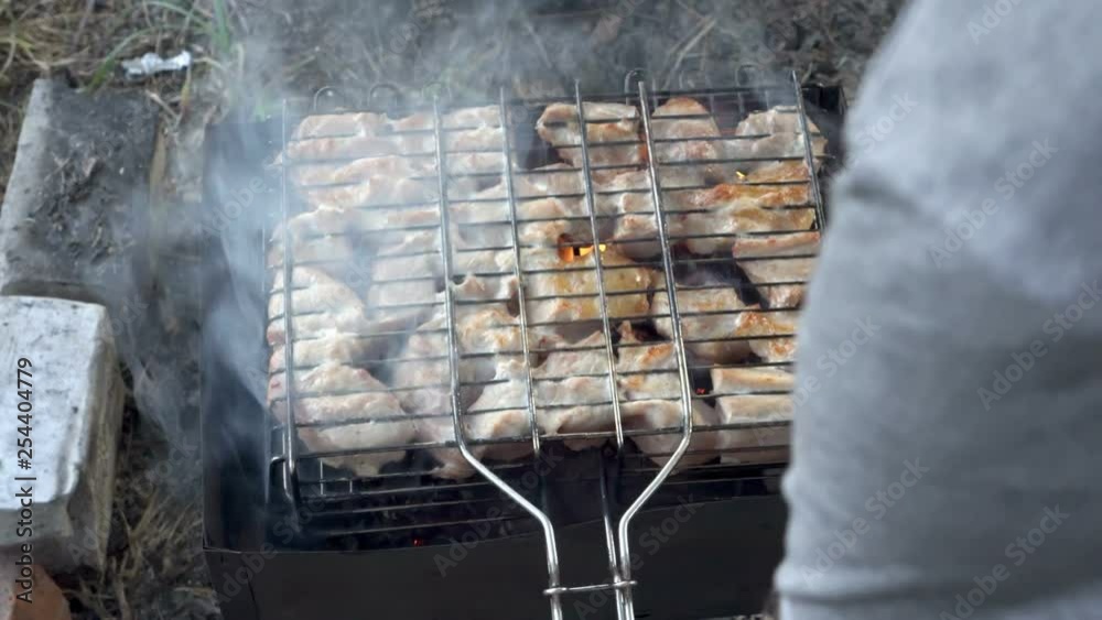 A man prepares barbecue outdoors. He roasts pieces of juicy meat on the coals. A picnic in the open air. Close up. The view from the top. 4k. 25 fps. A man prepares barbecue outdoors. He roasts pieces of juicy meat on the coals. A picnic in the open air. Close up. The view from the top. 4k. 25 fps.