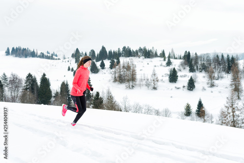 Young woman running on snow in winter mountains wearing warm clothing gloves in snowy weather