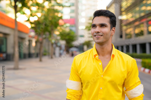 Happy young handsome Indian man thinking in the city street