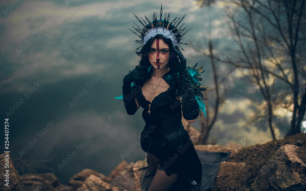 A woman in the image of a fairy and a sorceress standing over a lake in a black dress and a crown.