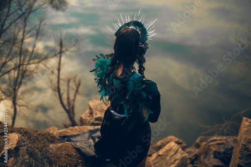 Fotografia A woman in the image of a fairy and a sorceress standing over a lake in a black dress and a crown