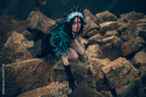 A young woman in the image of a fairy and a sorceress sitting on rock.