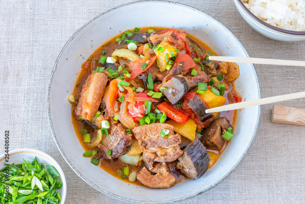 Fried pork with eggplants and sweet peppers in a large bowl and a cup of rice - a traditional Asian dish Fried pork with eggplants and sweet peppers in a large bowl and a cup of rice - a traditional Asian dish