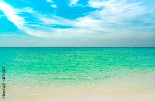 Golden sand beach by the sea with emerald green sea water and blue sky and white clouds. Summer vacation on tropical paradise beach concept. Ripple of water splash on sandy beach. Summer vibes. © Artinun