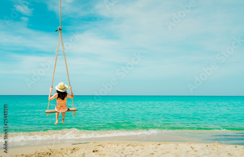 Asian woman wear swimwear and hat swing the swings at sand beach  and looking beautiful tropical paradise sea and sky on sunny day. Summer vacation. Summer vibes. Enjoying and relaxing girl on holiday © Artinun