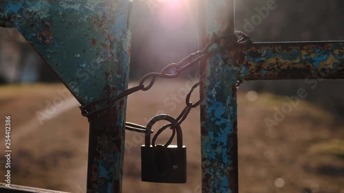 The sun's rays illuminate the old rusty lock on the chain, which closed the entrance gate