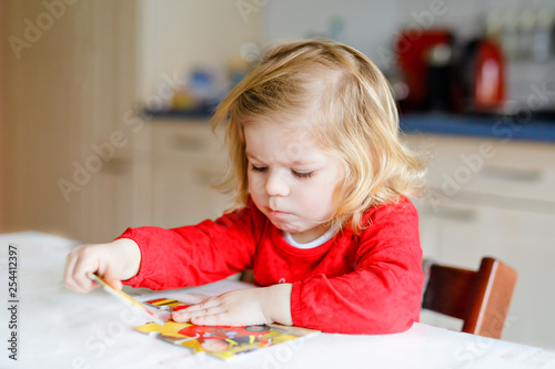 Adorable little toddler girl blonde child, playing with puzzles at home or kindergarten. Cute happy healthy child puzzling and making picture. Development and education step for baby