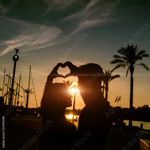 Silhouette of happy young couple love outside   showing hearts on hands. Twilight