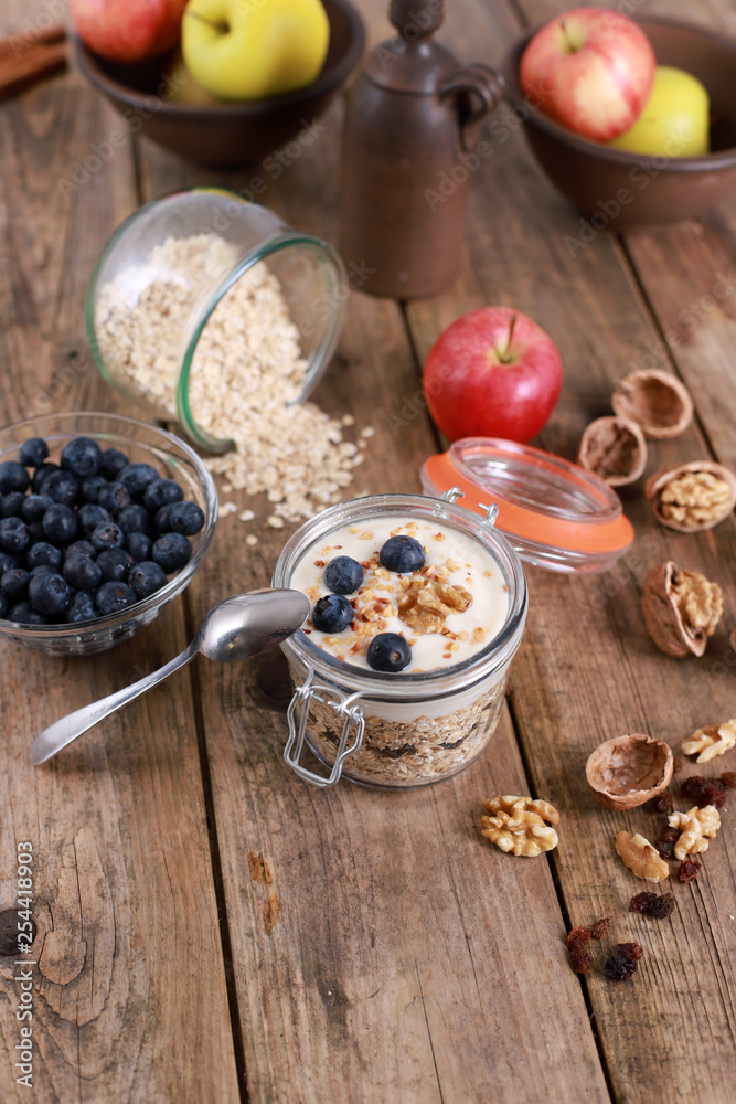 Fototapeta premium light healthy breakfast with yogurt on oatmeal muesli , blueberries and walnuts in a glas on a rustic wooden table