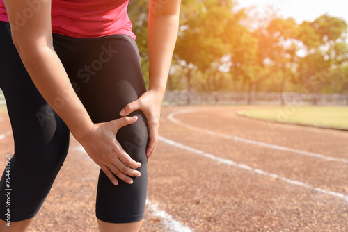 Young woman suffering from running knee or kneecap injury during outdoor workout on the stadium track in the morning.