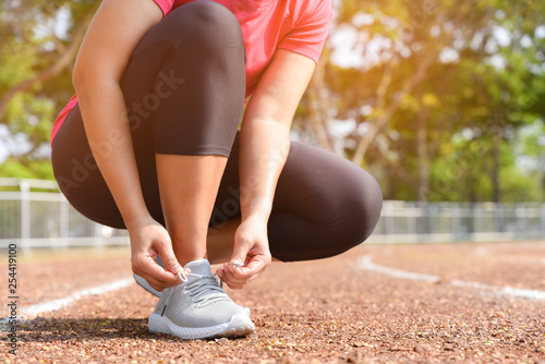 Closeup of young woman lacing running shoes for jogging outdoors on the stadium track. Fitness and healthy lifestyle concept.