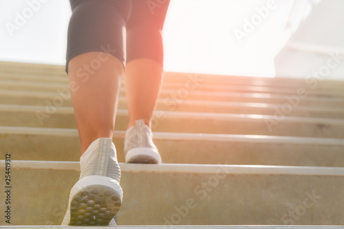 Young sport woman running up on stone stairs with sun spot background. Healthy lifestyle, workout and diet concept.