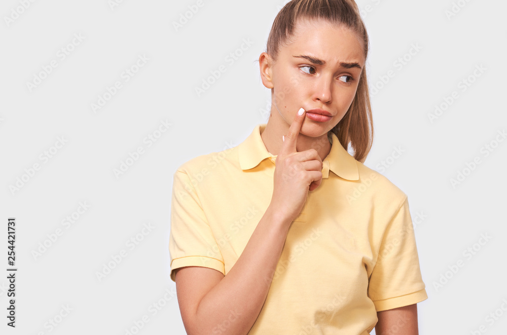 Thoughtful beautiful young woman thinking and looking upwards. Close up portrait of pretty confident female, holding finger near the face, looking seriously away posing over white background. People Thoughtful beautiful young woman thinking and looking upwards. Close up portrait of pretty confident female, holding finger near the face, looking seriously away posing over white background. People