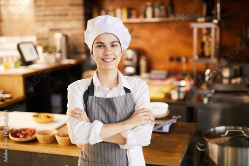 Waist up portrait of young cook smiling at camera while posing in restaurant kitchen, copy space photo