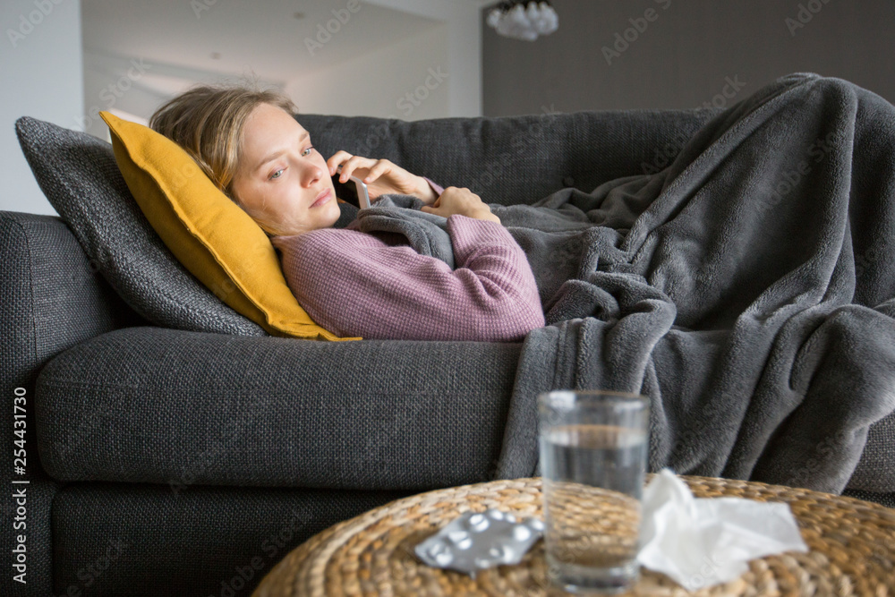 Obraz premium Sick woman lying on sofa and calling doctor on mobile phone